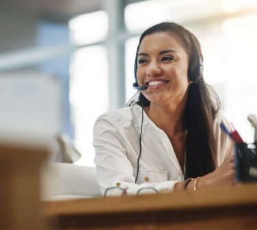 Smiling young woman looks at her computer and speaks into a headset - best call center jobs in Tijuana.